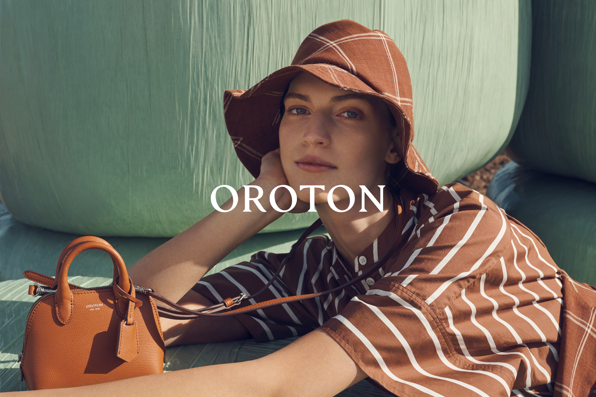 Vanessa Axente wearing a brown striped shirt and matching hat with a leather handbag for Oroton Summer campaign.