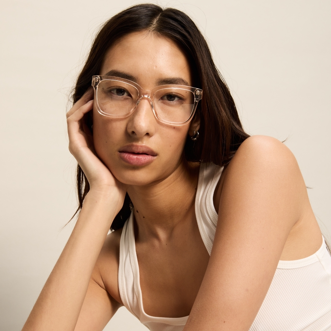 Model wearing clear frame glasses and a white tank top posing against a plain background