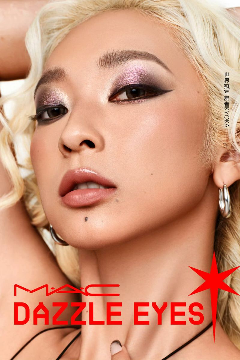 Close-up of a woman with blonde hair and striking eye makeup, showcasing the MAC Dazzle Eyes product line in a studio setting.