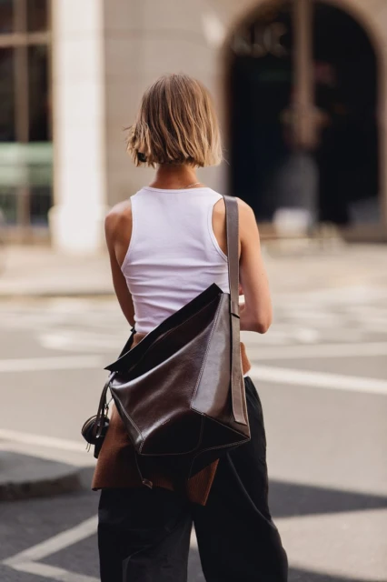 Back view of a woman with a brown leather shoulder bag walking in an urban setting; fashion and city life.