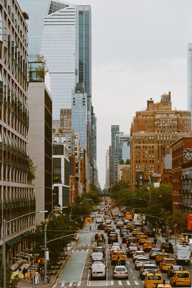 Urban landscape featuring a busy street filled with taxis and cars in New York City, surrounded by tall buildings under an overcast sky.