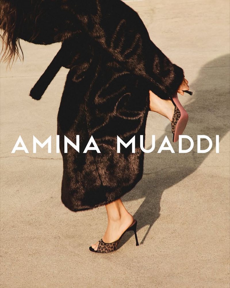 Fashion shot of a woman wearing a fur coat and patterned mules, showcasing style and design in an indoor setting with soft lighting.
