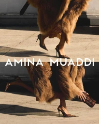 Model wearing a furry coat and stiletto pumps walking outdoors, photographed by Vito Fernicola for Amina Muaddi.
