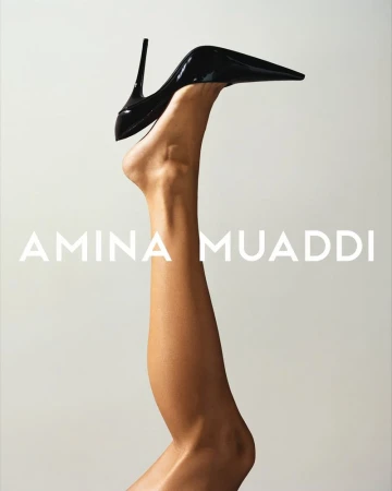 Close-up of a leg raised vertically wearing a glossy black stiletto heel pump against a minimal light grey background.