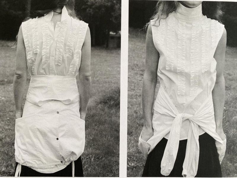 Monochromatic fashion shot of a woman wearing a white sleeveless top and skirt set against a grassy outdoor backdrop.  