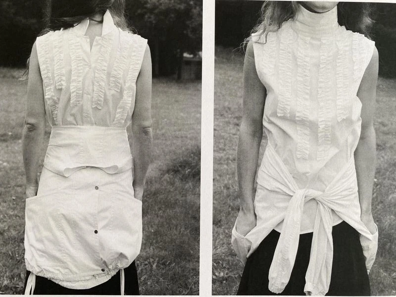 Monochromatic fashion shot of a woman wearing a white sleeveless top and skirt set against a grassy outdoor backdrop.  