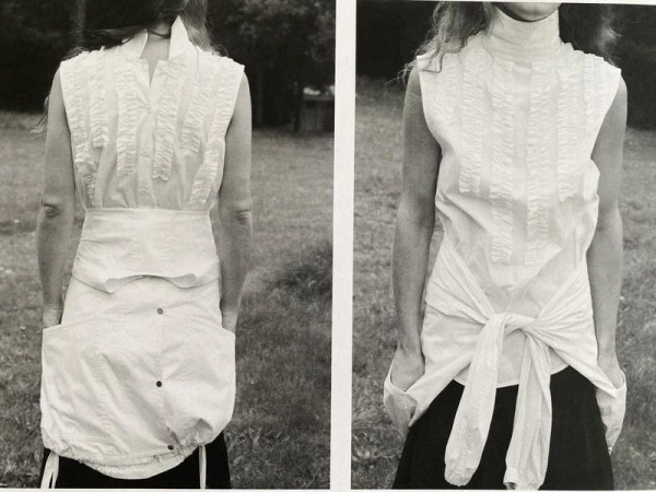 Monochromatic fashion shot of a woman wearing a white sleeveless top and skirt set against a grassy outdoor backdrop.  