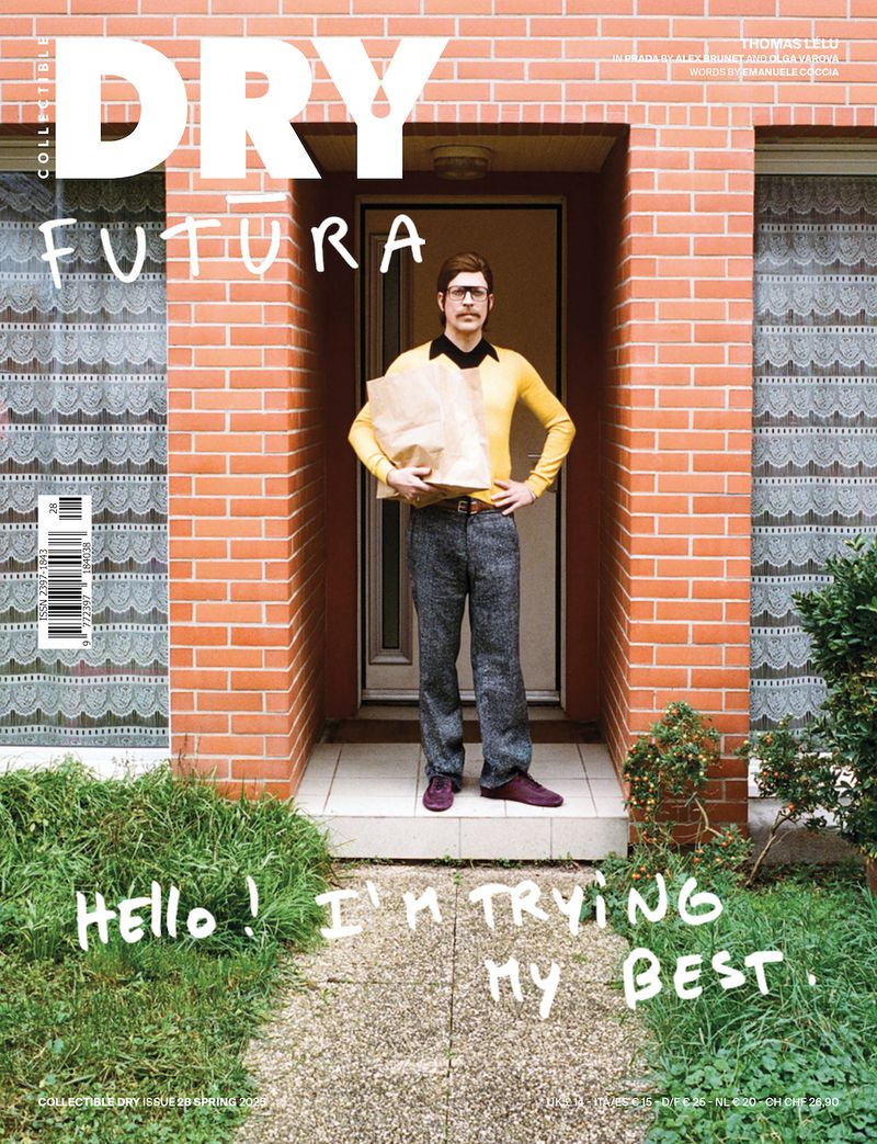 Magazine cover with a man in retro attire standing at a brick doorway holding a paper bag, with playful graffiti on the walkway.