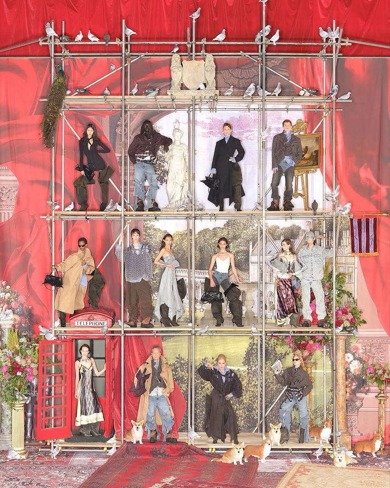 Multiple figures and corgis are on a scaffolding structure in front of a red curtain backdrop, creating a visually rich and complex fashion scene.
