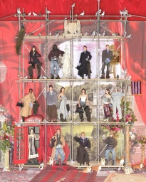 Group of models posed across a large metal scaffolding structure with red velvet curtains and corgi dogs in the foreground