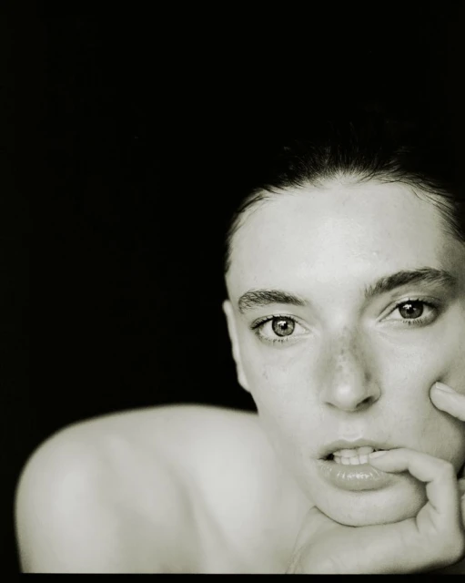 Close-up portrait of a fair-skinned young woman with dark hair and eyes, biting her lip against a dark background, shot in black and white.