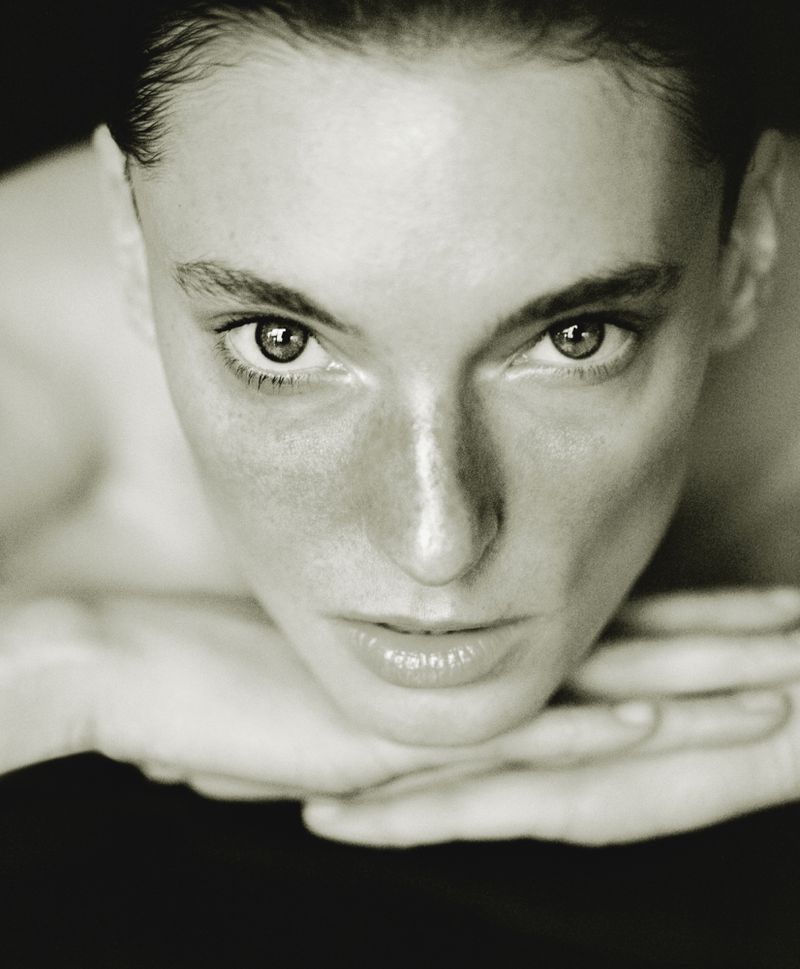 Close-up portrait of a woman resting her face on her hands against a dark background in AUNU Beauty Campaign