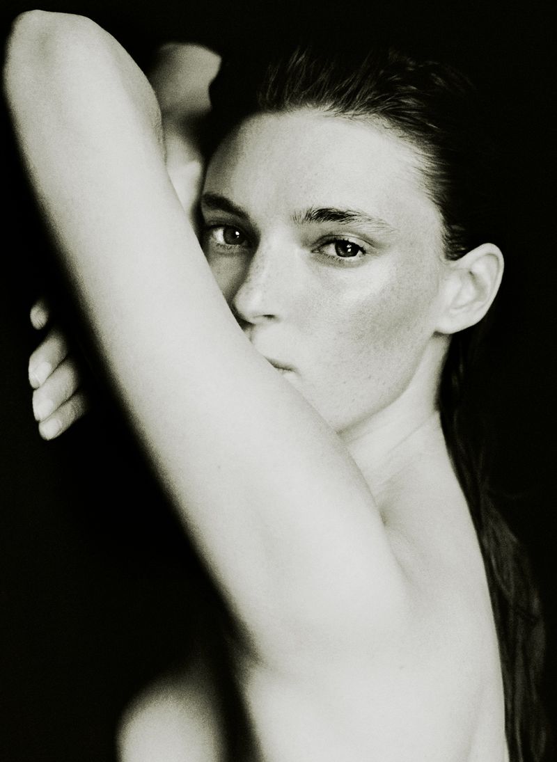 Close-up portrait of a woman with her arm raised, posing against a stark black background for the AUNU Beauty Campaign.