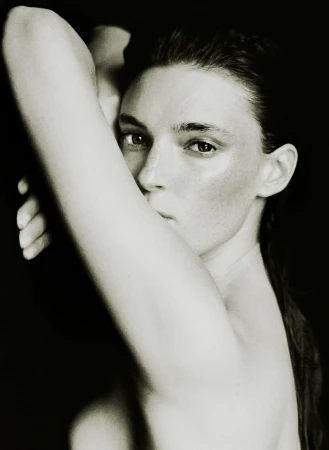 Close-up portrait of a woman with her arm raised, posing against a stark black background for the AUNU Beauty Campaign.