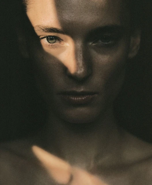 Portrait of a light-skinned woman with fair hair in a dark environment, one half of her face lit by stark natural sunlight.