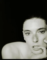 Close-up portrait of a woman resting her chin on her hand against a dark background for AUNU Beauty Campaign
