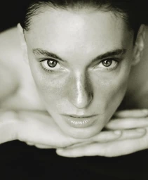 Close-up portrait of a woman resting her face on her hands against a dark background in AUNU Beauty Campaign