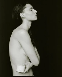 Profile portrait of a woman holding a white beauty jar against a black background for the AUNU Beauty Campaign