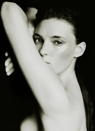 Close-up portrait of a woman with her arm raised, posing against a stark black background for the AUNU Beauty Campaign.