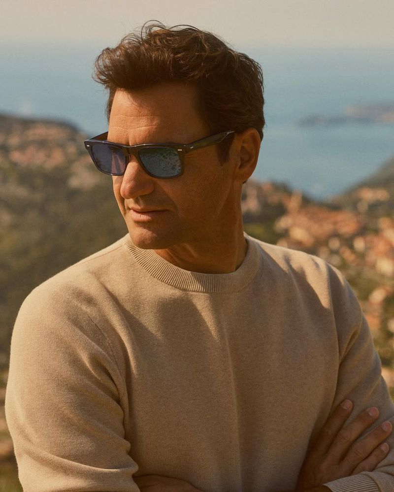 Roger Federer wearing Oliver Peoples sunglasses and a beige sweater outdoors with coastal background