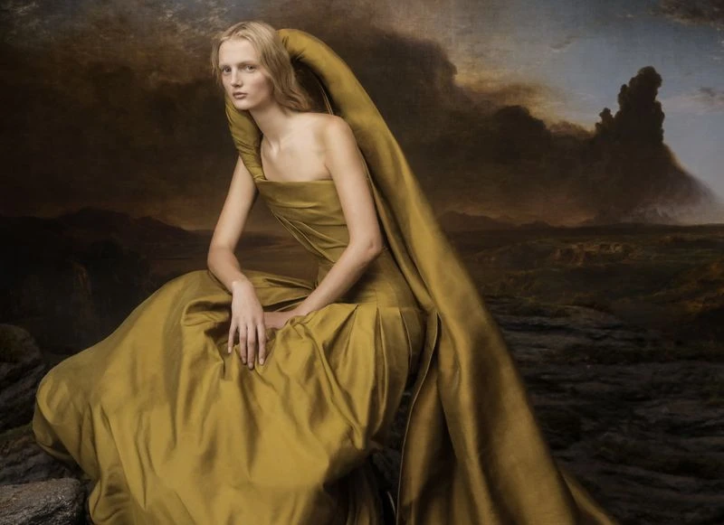 Woman in yellow dress posing against a landscape background, creating a visually striking fine-art fashion image with a dramatic backdrop.