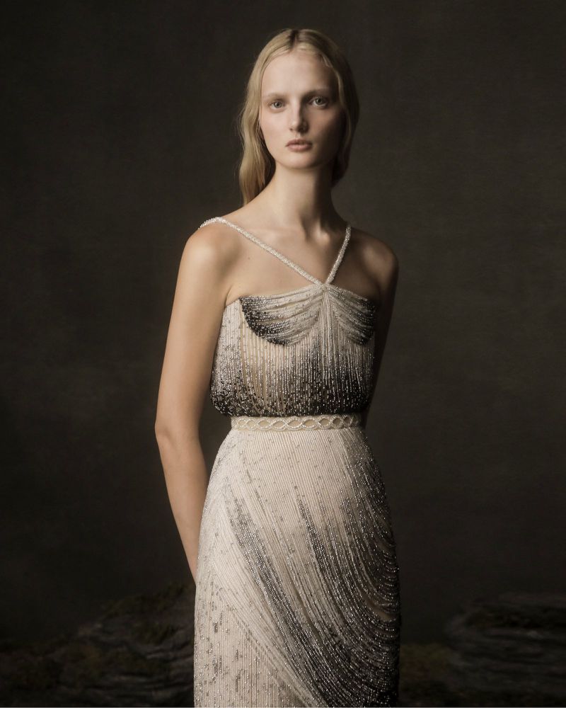Woman in beaded gown posing against a muted background. Fashion shot with detailed textures and soft lighting for editorial use.