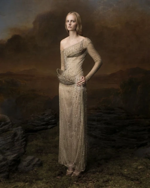 Full-length shot of a blonde adult female wearing a gold beaded gown with landscape background, fashion editorial.