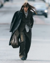 Model Aylah Peterson walking on a city street wearing a dark tailored suit and coat, carrying a leather handbag for Net-A-Porter REACTIVE.
