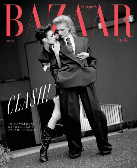 Two fashion models pose in a black-and-white Harper's Bazaar Italia cover shoot, wearing dark business suits against a neutral backdrop.