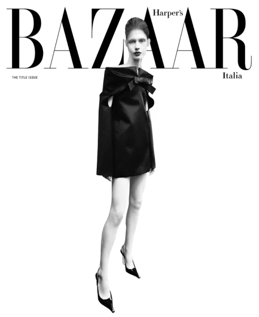Fashion editorial cover featuring a full-length shot of a woman in a black dress and heels against a clean, bright white backdrop.