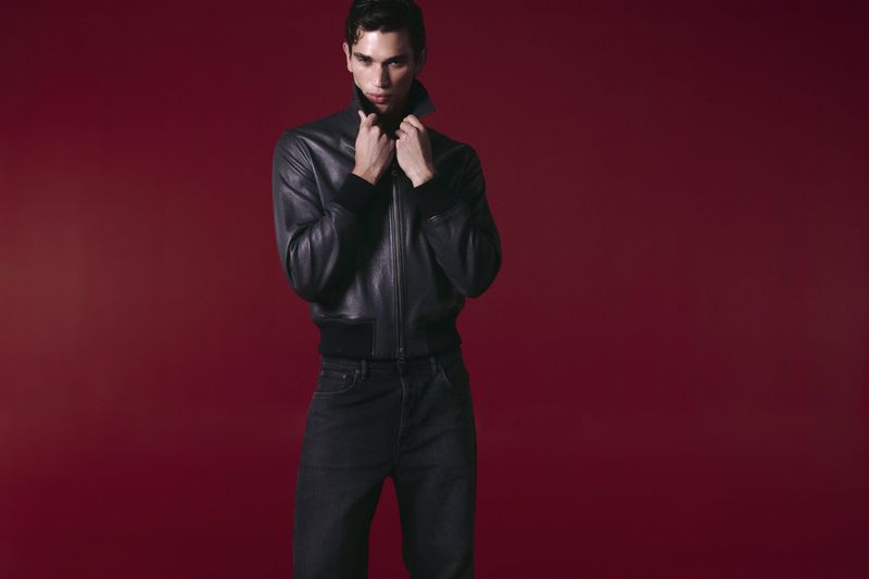 Model Mauria Caetano in a black leather jacket and dark jeans against a deep red seamless studio background.
