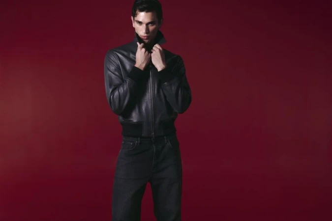 Model Mauria Caetano in a black leather jacket and dark jeans against a deep red seamless studio background.