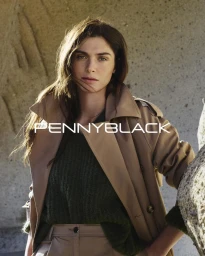Model Elisa Sednaoui wearing a camel trench coat and green knit sweater against a rocky background for Pennyblack.