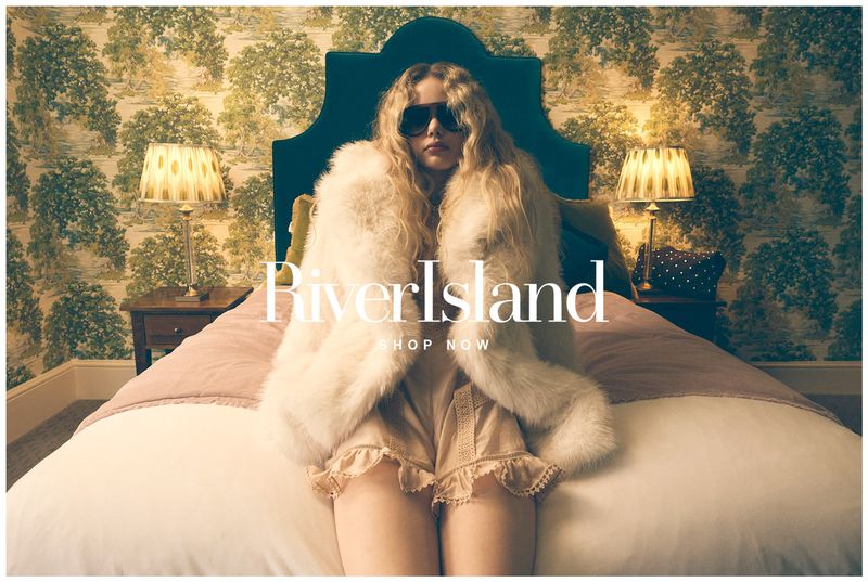 A fashion shot features a woman wearing sunglasses and a fur coat, sitting on a bed with a patterned headboard and wallpaper.