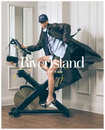 Model wearing a brown leather jacket and cap seated on an exercise bike in an interior room