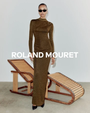 Model Ana Beatriz Cortes wearing a long bronze metallic dress and sunglasses standing beside a wooden lounger