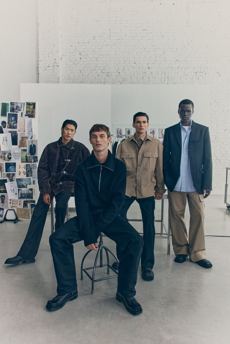 Group of four male fashion models in studio wearing casual jackets and trousers in a bright minimalist studio. 