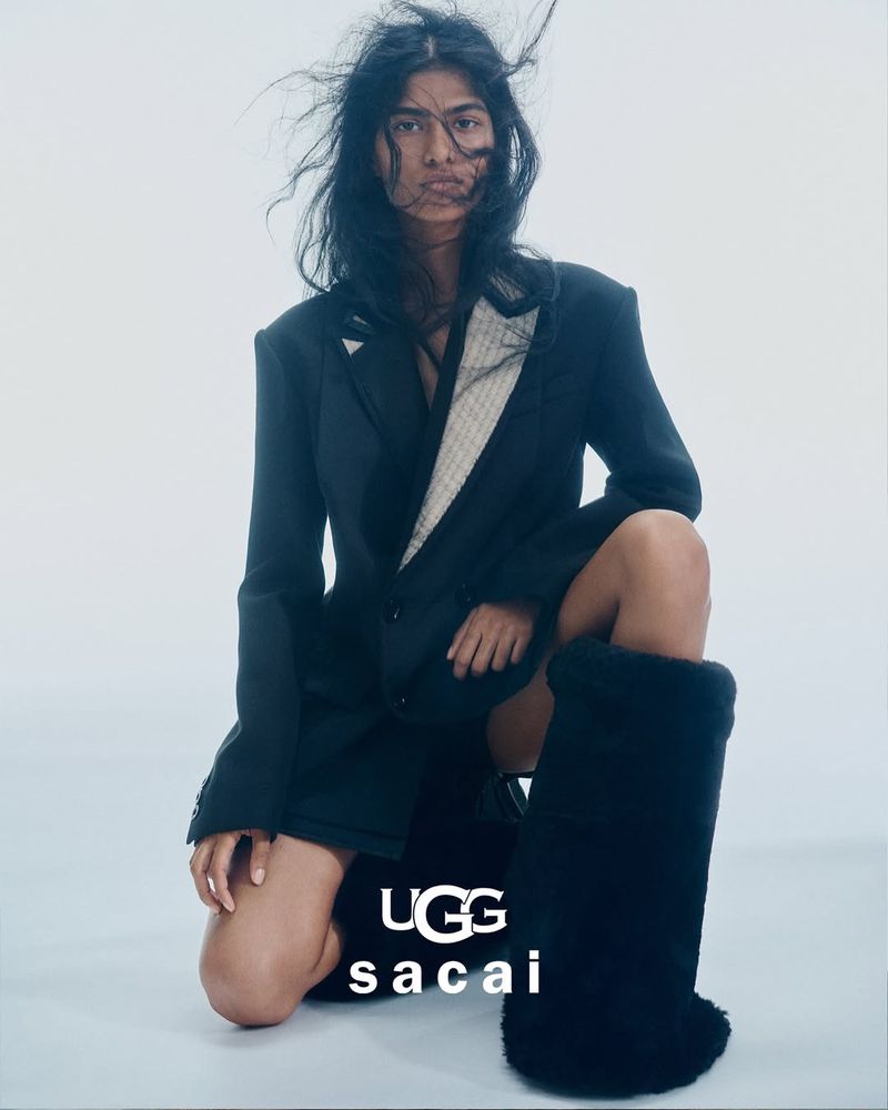Fashion model in a black blazer and oversized UGG boots kneeling against a white backdrop in a studio environment for a style editorial.
