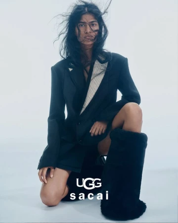 Fashion model in a black blazer and oversized UGG boots kneeling against a white backdrop in a studio environment for a style editorial.