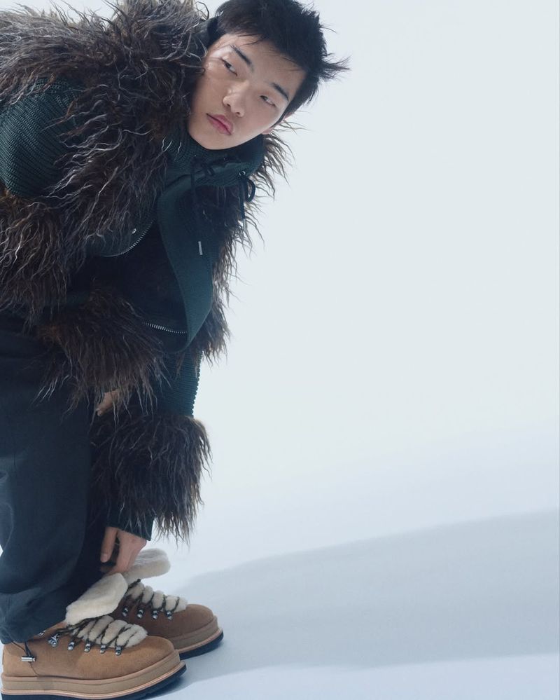 Man in fashionable winter clothing. He is wearing a fur trimmed jacket and lug soled boots against a stark white backdrop.