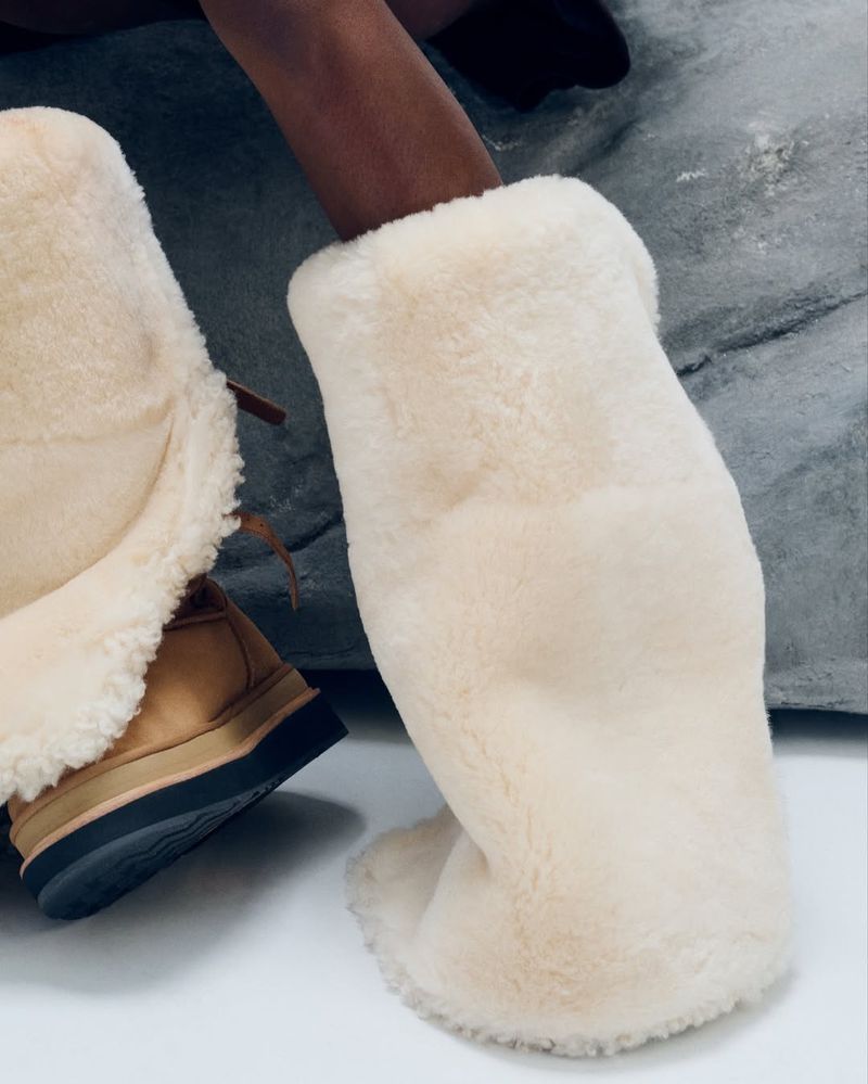 A pair of fur-lined boots in a well-lit studio setting, showcasing their tan and cream color scheme and plush texture.