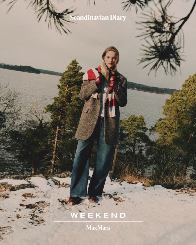 Fashion editorial shot of a model in an outdoor winter environment with a water view, wearing a wool coat and jeans, styled with a scarf.