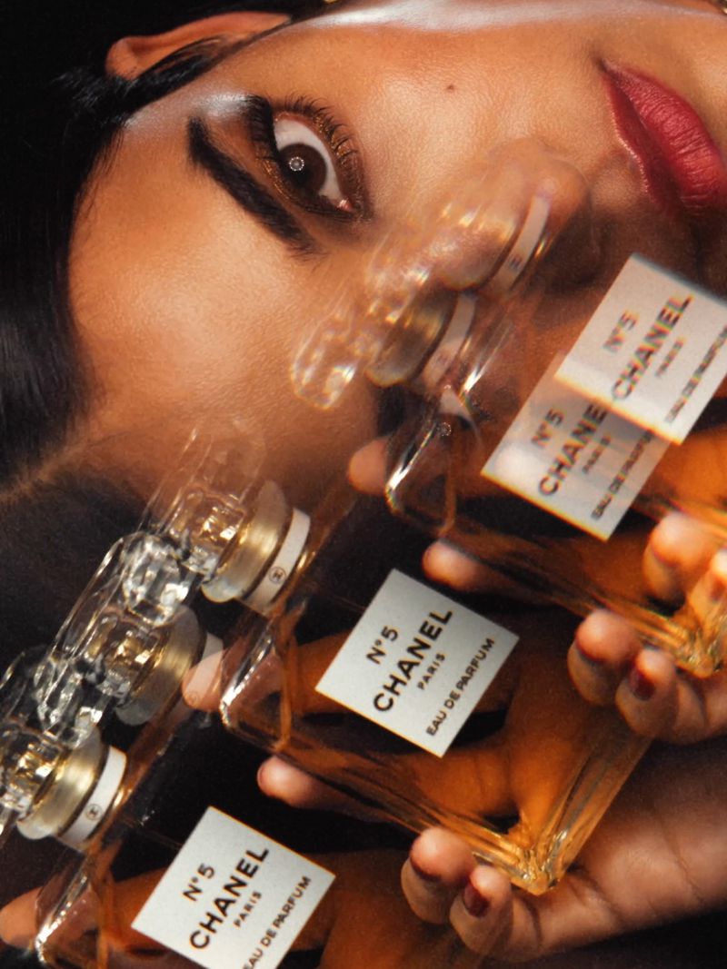 Close-up of a woman's face with red lipstick, partially blurred, with multiple Chanel No. 5 perfume bottles in the foreground.
