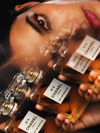 Close-up of a woman's face with red lipstick, partially blurred, with multiple Chanel No. 5 perfume bottles in the foreground.