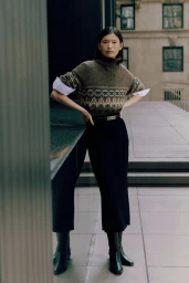 Model Cecilia Wu wearing a patterned knit sweater, black midi skirt, and black leather boots on an urban terrace.