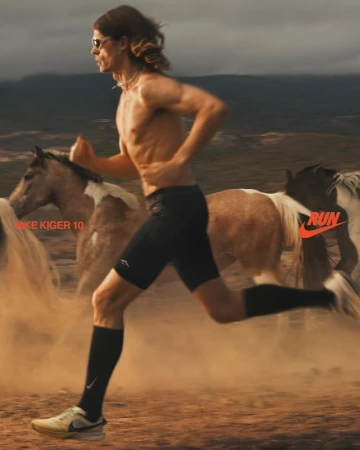 Athletic man running barefoot with horses in a desert landscape wearing Nike gear with a Nike logo, emphasizing motion and athleticism.