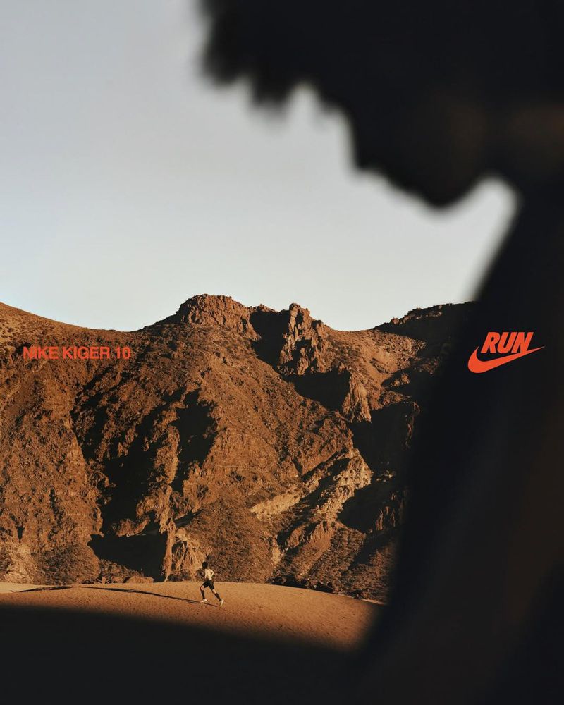 Runner on desert terrain with mountain backdrop and partial human silhouette featuring the Nike swoosh and 'RUN' text.