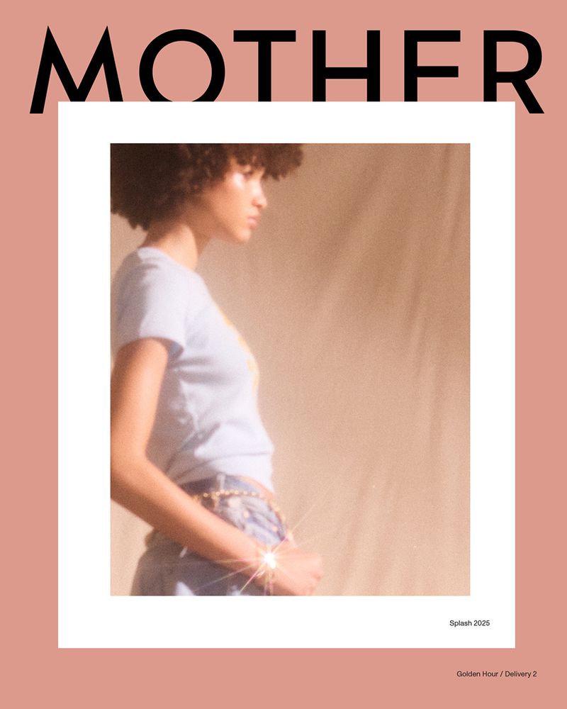Fashion editorial shot of a young adult female model with curly hair, wearing a light blue top and jeans, on a peach background.