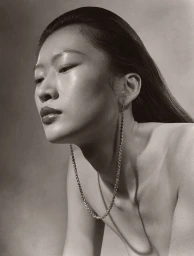 Close-up portrait of an East Asian model wearing a long chain necklace against a textured neutral background, photographed by Paul Kooiker.