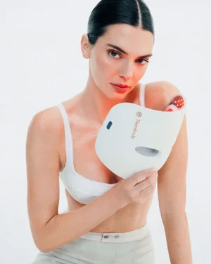 Kendall Jenner holding a white Therabody TheraFace LED mask against a clean white studio backdrop.
